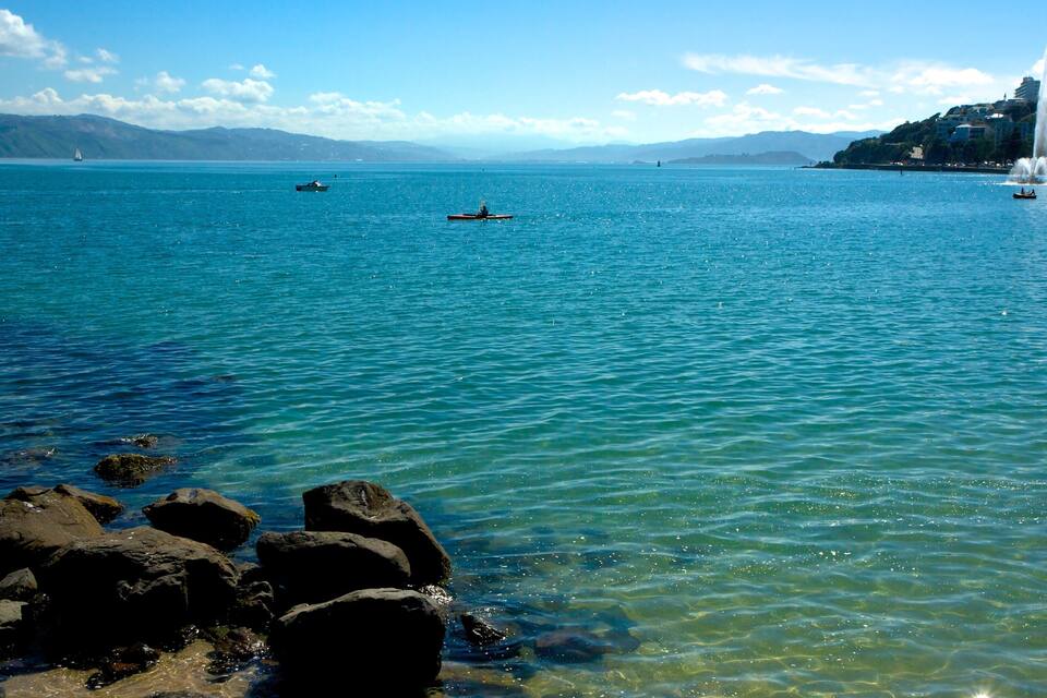 Une mer d’un bleu profond, parsemée de bateaux, une côte rocheuse et une fontaine.