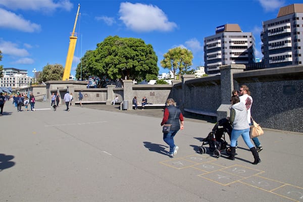 A public square with people walking, a yellow tower, and modern buildings.