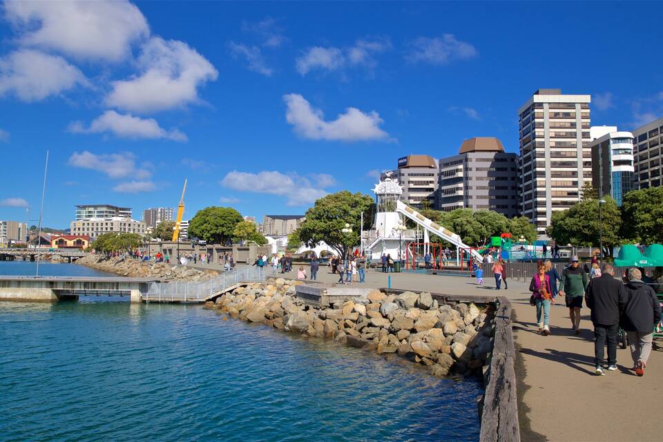 A waterfront promenade with a rocky breakwater, a playground, and modern buildings in the background.