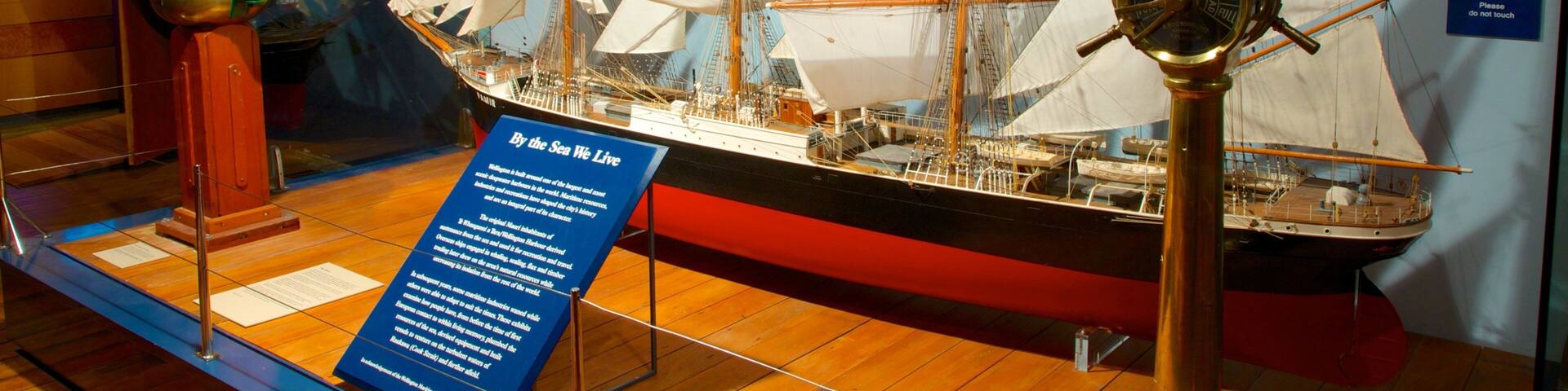 Una exposición de museo marítimo que muestra un gran barco de vela con múltiples mástiles y velas, una rueda de timón de bronce y paneles informativos.