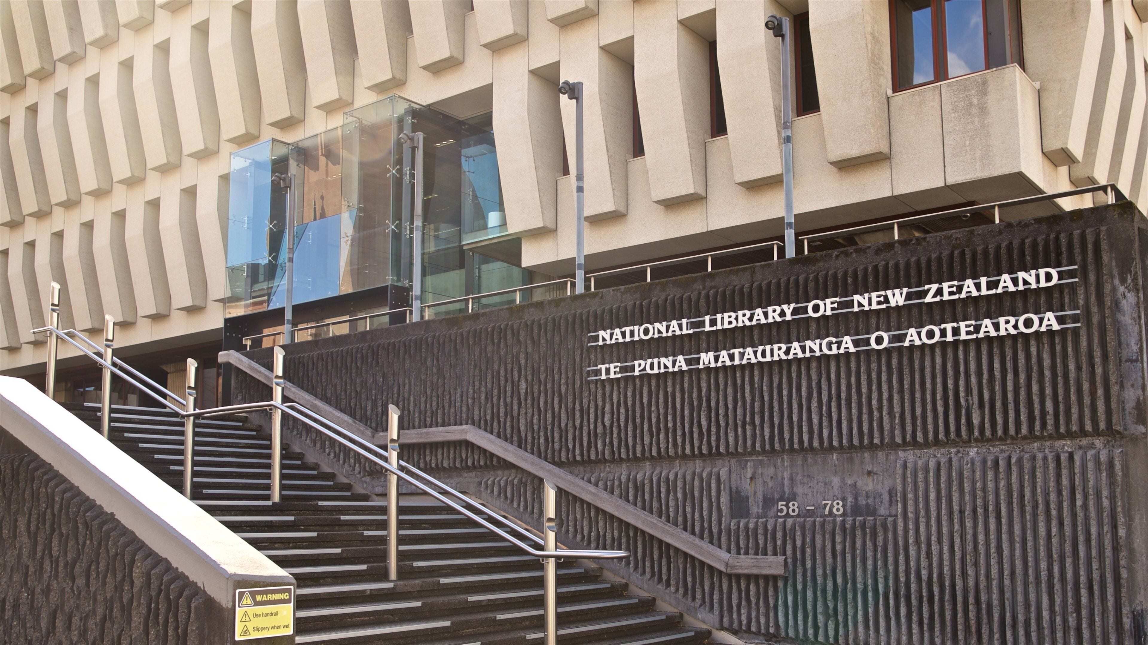 A staircase leading to the National Library of New Zealand, Te Puna Matauranga o Aotearoa, with a warning sign about slippery steps.