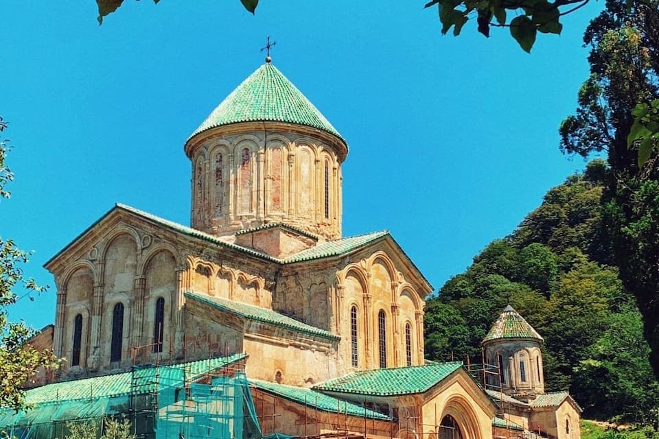 A historic church with a prominent central dome and smaller domes, surrounded by lush greenery.