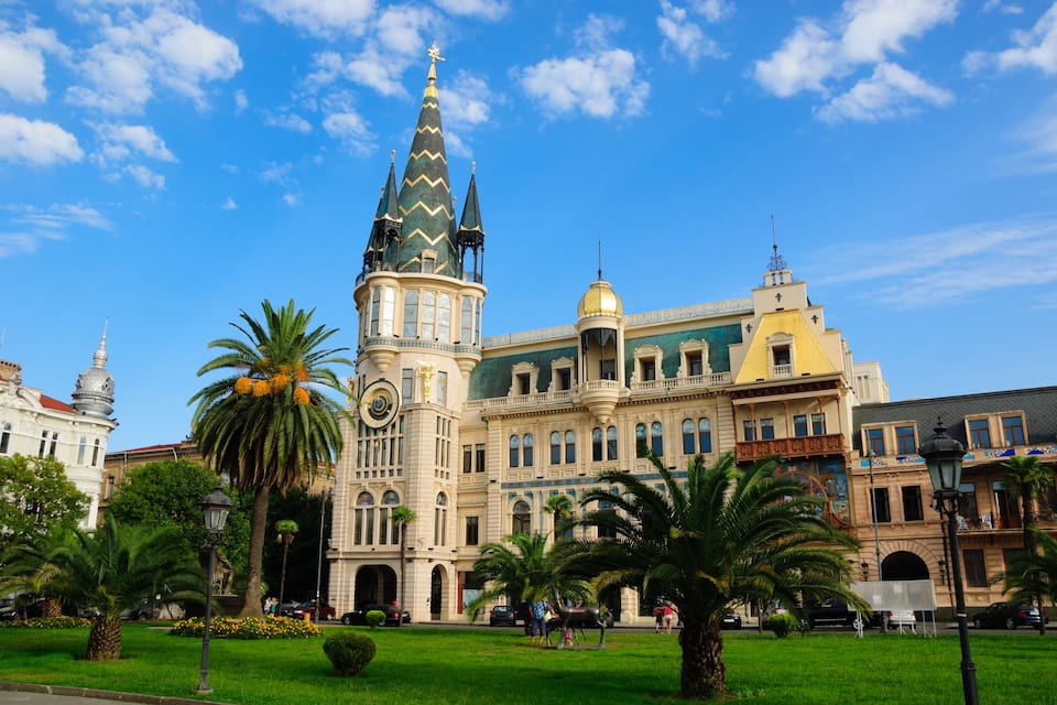 Un edificio histórico con una torre alta y una cúpula, rodeado de palmeras y un cielo azul despejado.