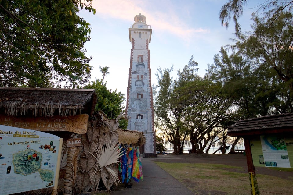 A tower with a clock, surrounded by trees and a signboard.