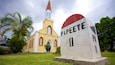 A church with a red steeple and a gravestone labeled "Papeete" in front of it.