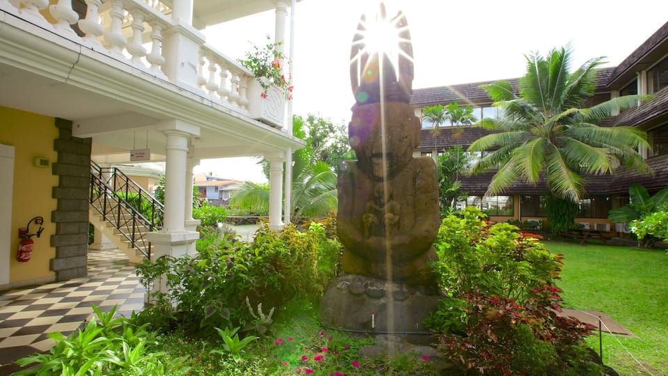 A courtyard with a stone statue, lush greenery, a checkered floor, and a white building with balconies.
