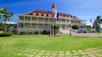 A large colonial-style building with a red roof and white columns, surrounded by well-maintained lawns and palm trees.