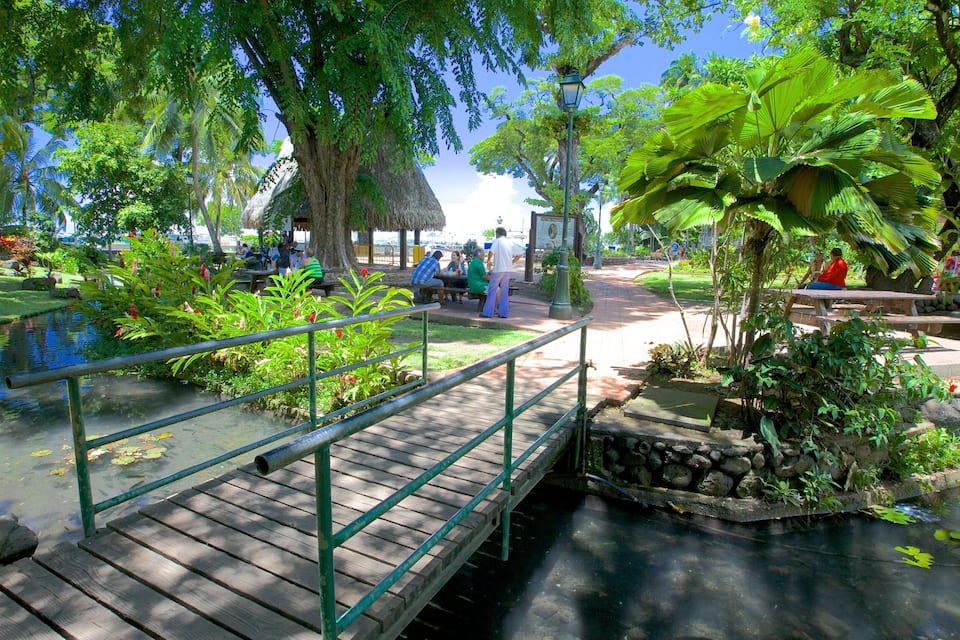 A wooden bridge over a calm waterway, surrounded by lush greenery and trees.