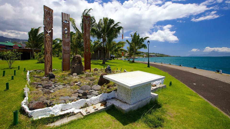 A landscaped area with palm trees, a stone monument, and a view of the ocean.