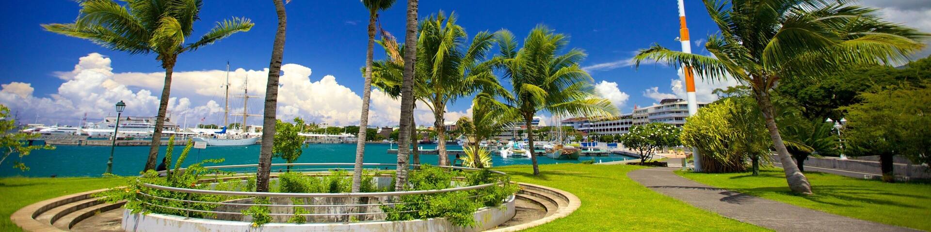 A coastal park with palm trees, a lighthouse, and a marina with boats.