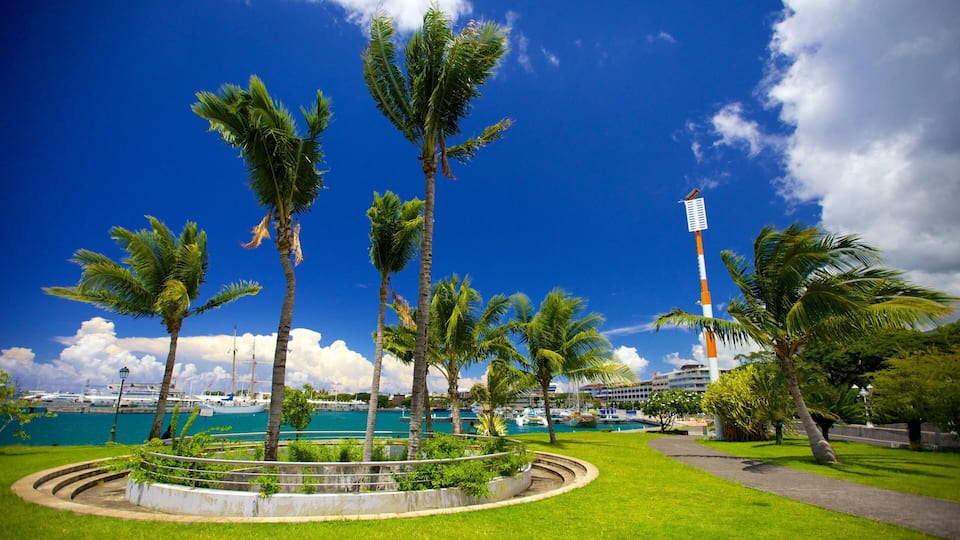 A coastal park with palm trees, a lighthouse, and a marina with boats.