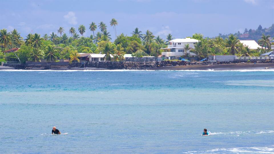 A beach with two people in the water, palm trees, and houses along the shore.