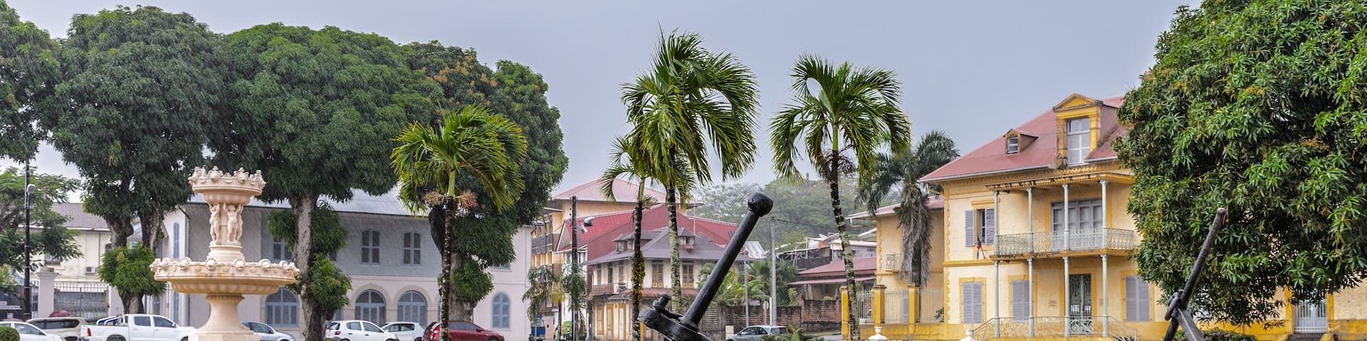 A park with a fountain, palm trees, and a statue of an anchor.