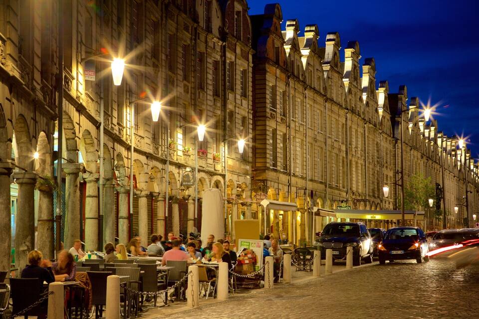 A historic European street at night with illuminated buildings and outdoor seating for cafes.