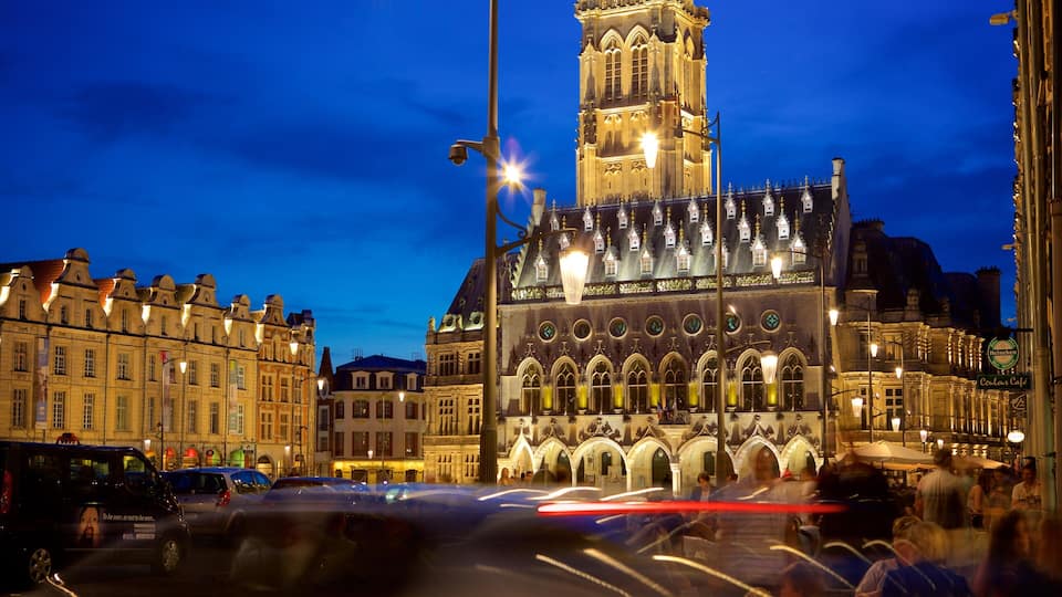 A historic building with a clock tower, illuminated windows, and a busy street with cars.