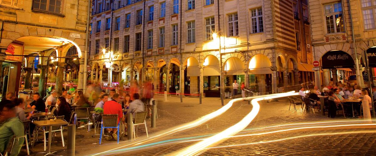 A cobblestone street with historic buildings and outdoor cafes at dusk.