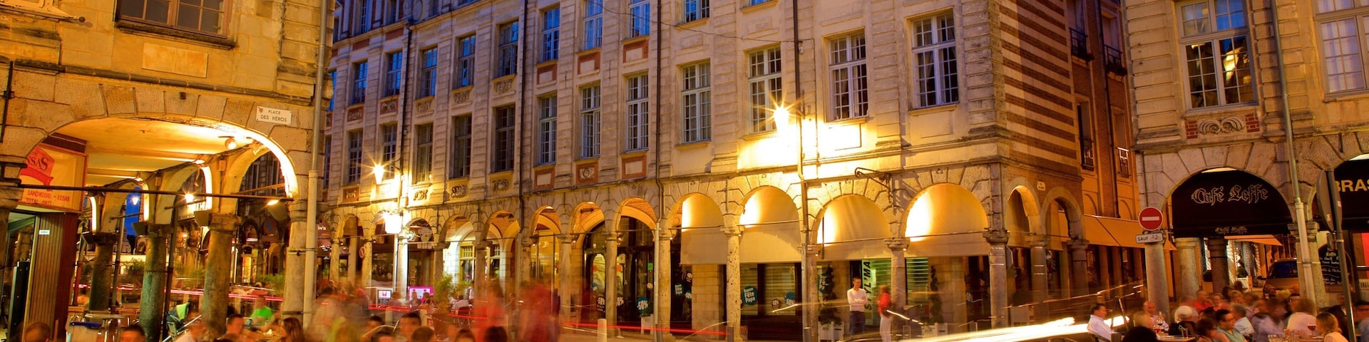 A cobblestone street with historic buildings and outdoor cafes at dusk.