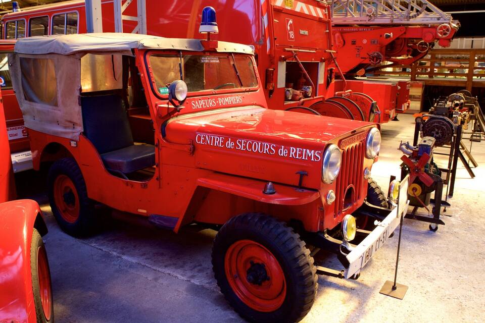 En ældre rød brandbil med teksten "CENTRE de SECOURS de REIMS" på, parkeret i en garage.