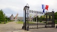 Een ijzeren hek met de naam 'POMMERY' in gouden letters, een Franse vlag en een gebouw met een toren op de achtergrond.