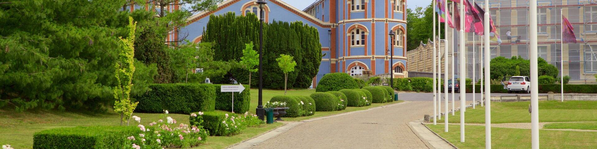 A pathway leading to a historic building with a tower, surrounded by well-maintained gardens and flags.