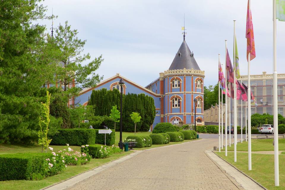 A pathway leading to a historic building with a tower, surrounded by well-maintained gardens and flags.