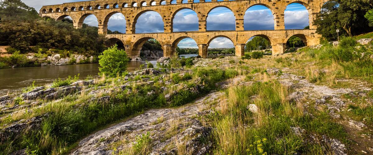 A stone aqueduct with multiple arches over a river, surrounded by greenery and rocks.