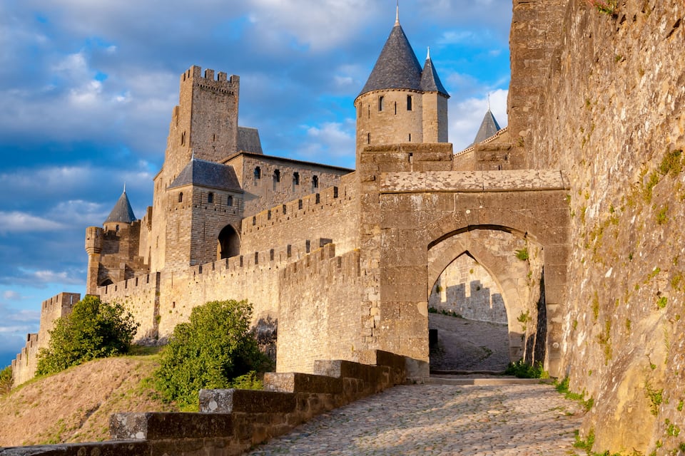 Un castillo de piedra histórico con múltiples torres y un camino empedrado que lleva a una entrada arqueada.
