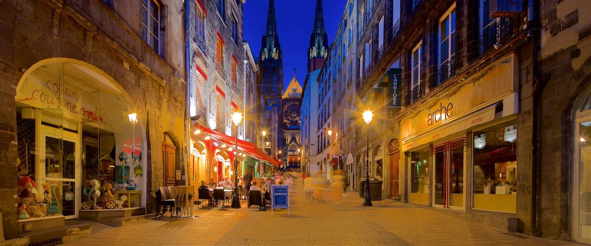 A nighttime street scene with historic buildings, illuminated signs, and a prominent church spire in the background.