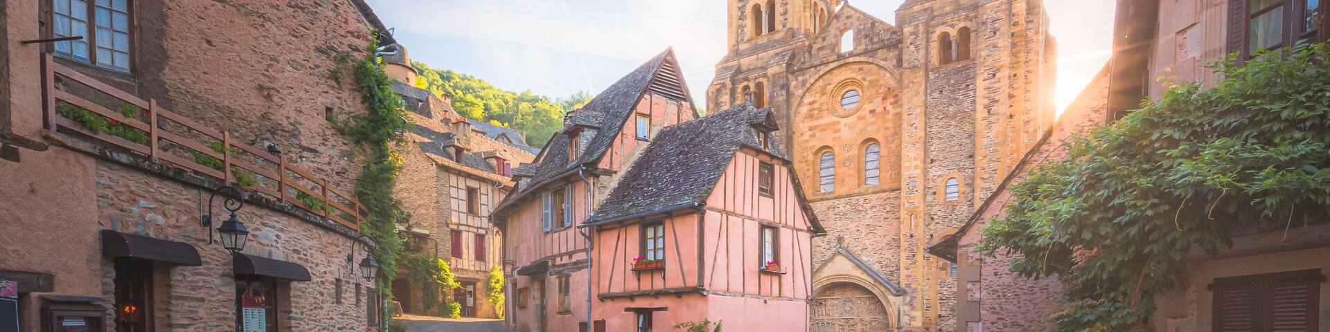 The quaint and charming town centre of the medieval French village Conques, Aveyron and Abbey Church of Sainte-Foy at sunset or sunrise in Occitanie, France.