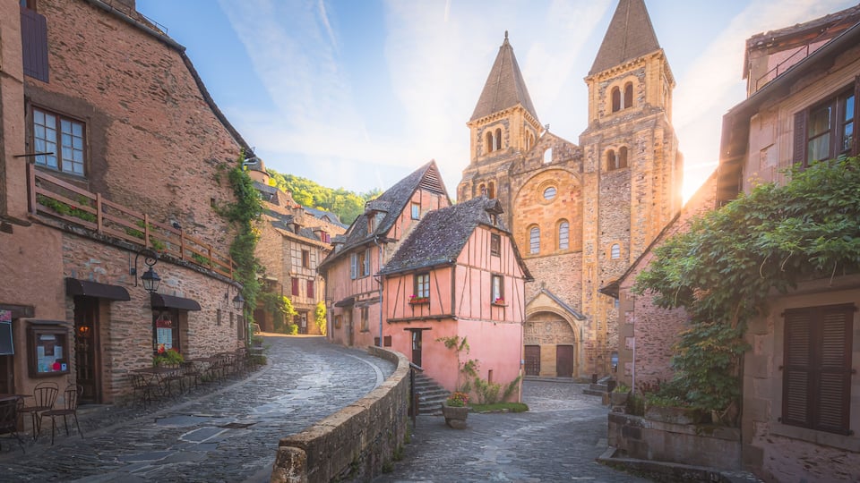 The quaint and charming town centre of the medieval French village Conques, Aveyron and Abbey Church of Sainte-Foy at sunset or sunrise in Occitanie, France.