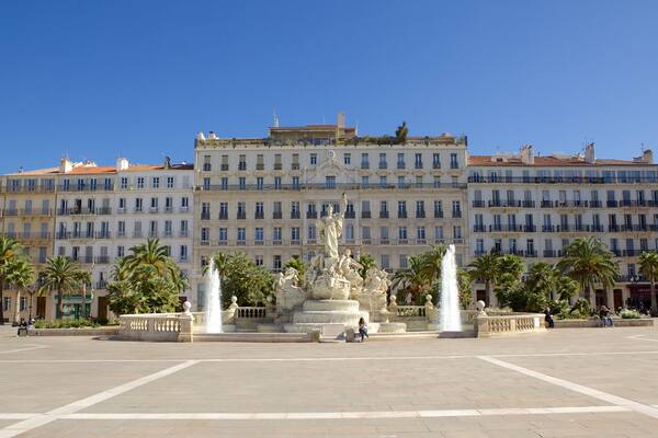 A plaza with a large fountain, palm trees, and historic buildings in the background.