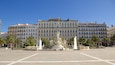 A plaza with a large fountain, palm trees, and historic buildings in the background.