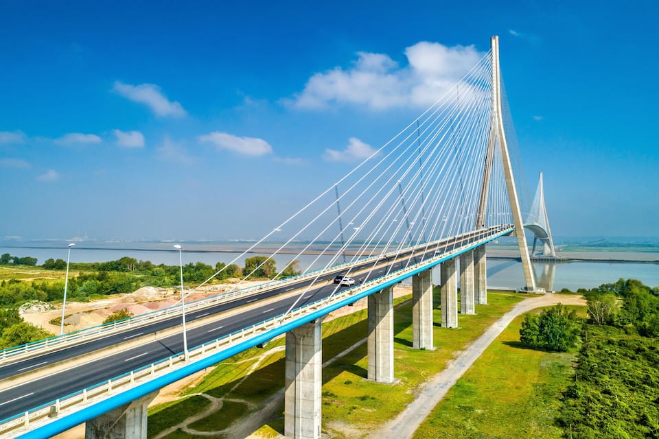 A cable-stayed bridge with a blue deck, large concrete pillars, and a clear blue sky.