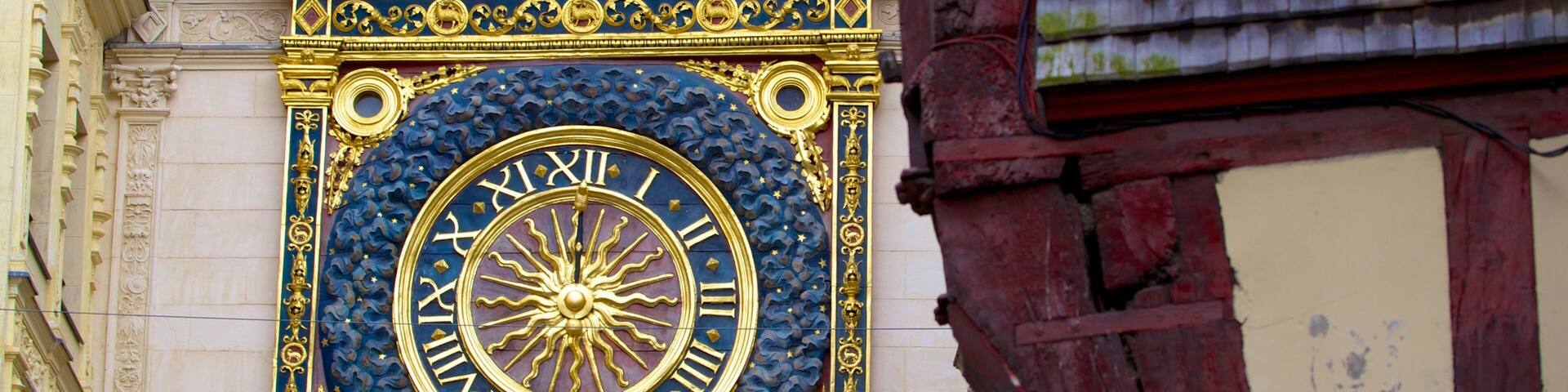 A detailed, ornate clock with Roman numerals and a sun motif, set against a building facade with classical architectural elements.