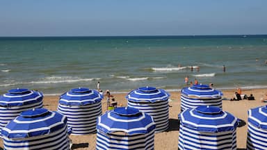 Une plage avec des parasols bleus et blancs à rayures, et des gens qui se baignent dans l’eau.