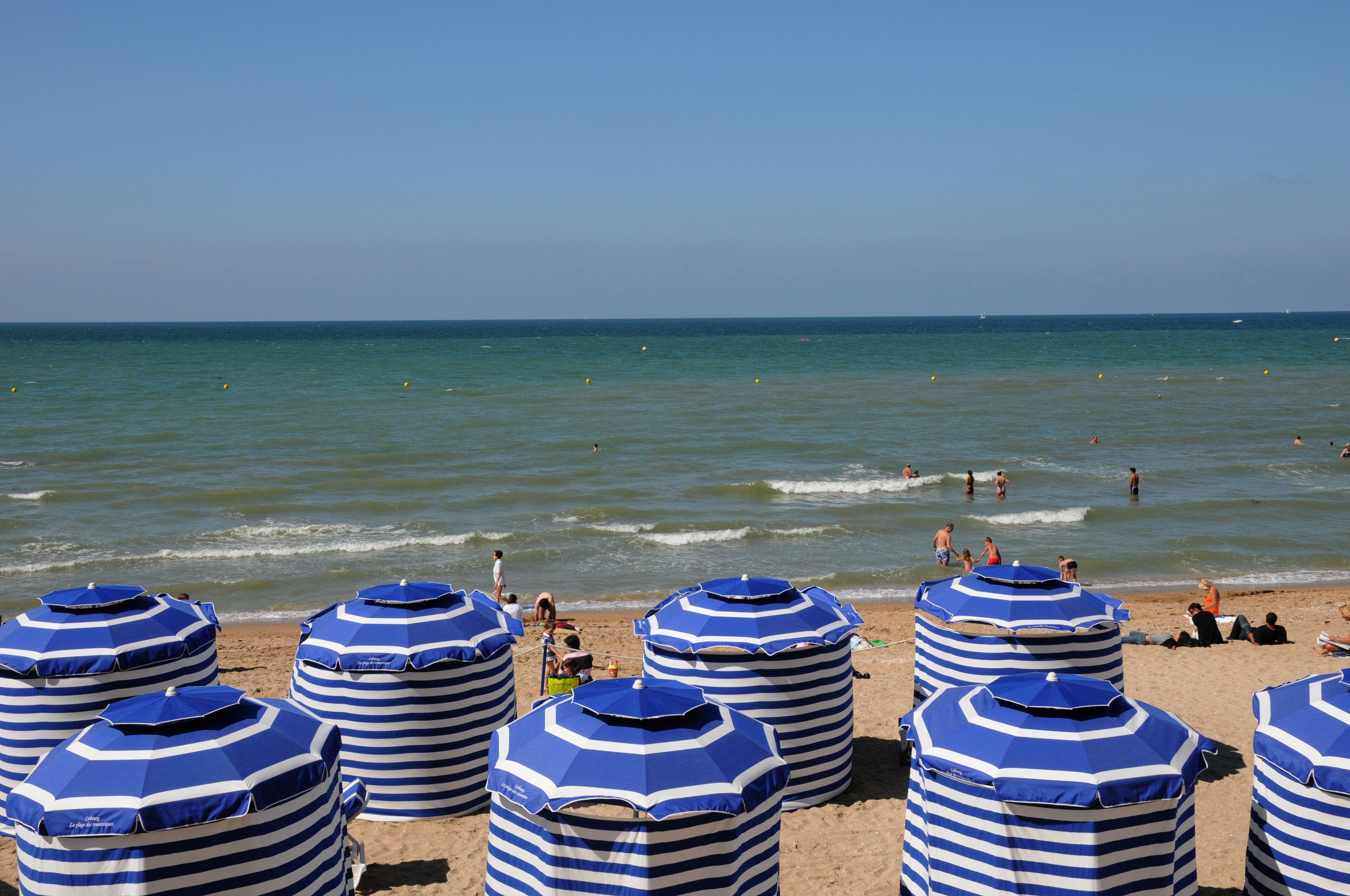 A beach with striped blue and white umbrellas and people swimming in the water.