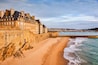 Une ville côtière dotée d’une plage de sable, d’un mur de pierre et d’une rangée de bâtiments historiques situés au bord de l’eau.
