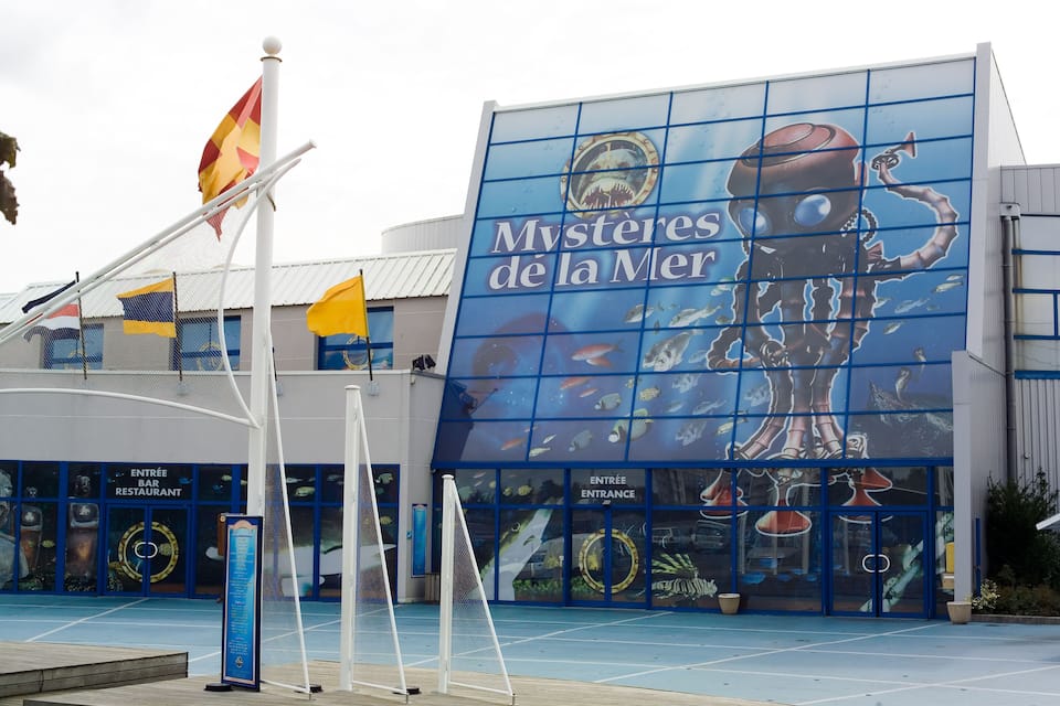 Un edificio con un gran mural de un pulpo y el texto "Mystères de la Mer". Hay banderas y un letrero para un bar y restaurante de entrada.