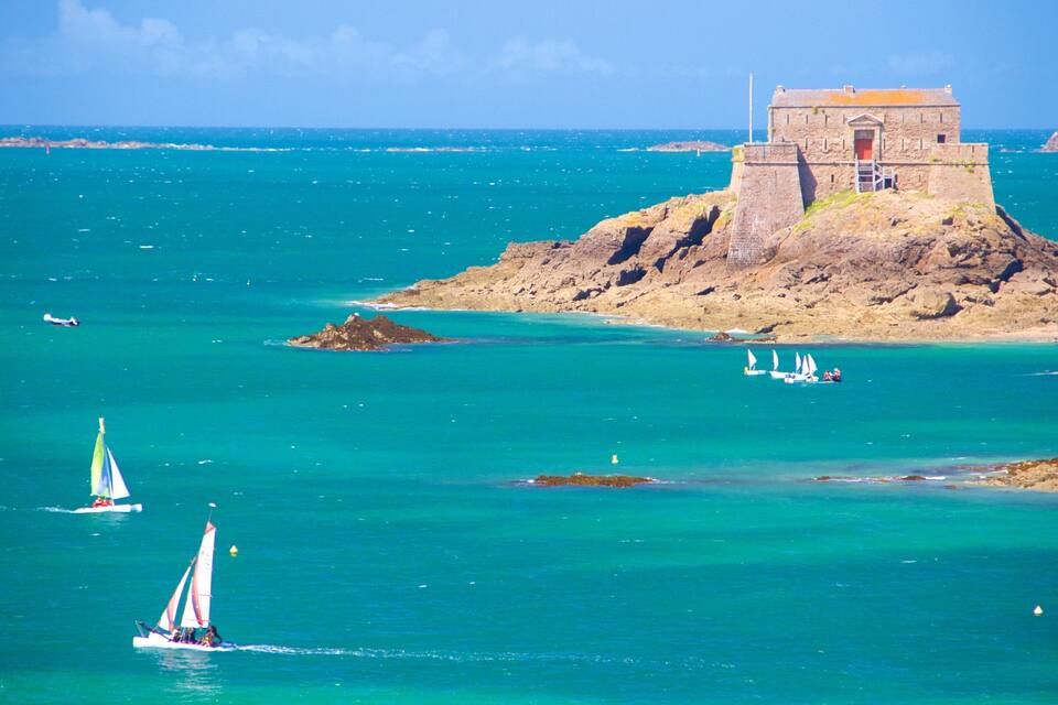 A coastal scene with a lighthouse, a small island with a building, and sailboats on the water.