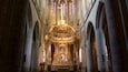 Interior de una catedral con una gran cruz, vidrieras y un altar ricamente decorado.