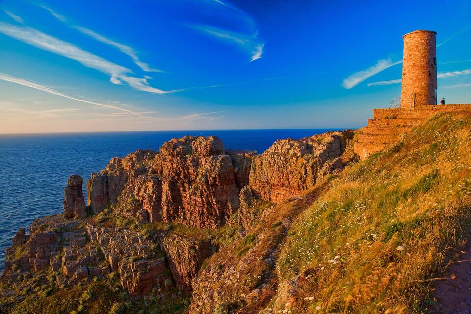 A coastal cliff with a lighthouse, rocky formations, and the sea.