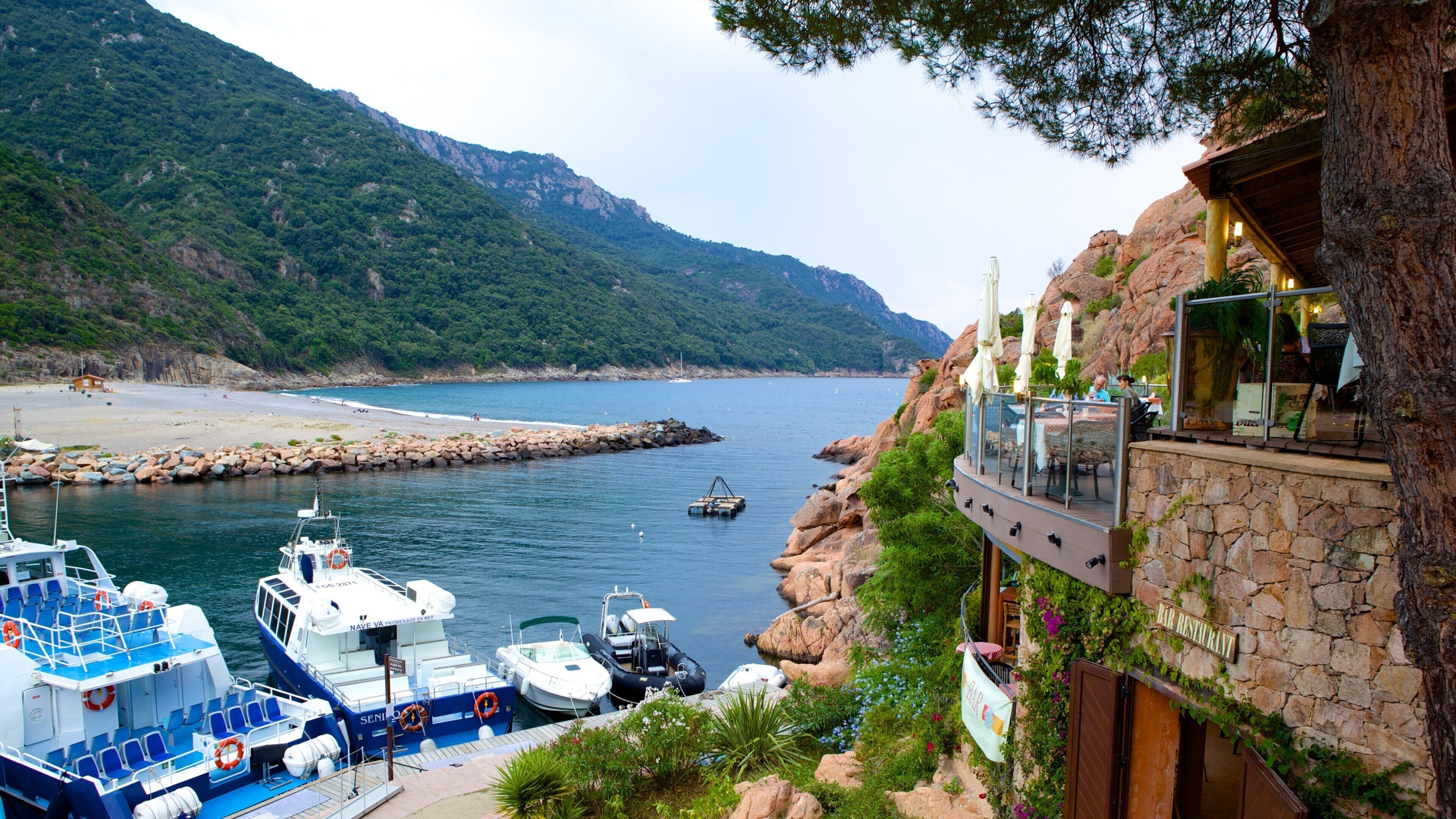 A coastal area with boats docked, a rocky shoreline, and a restaurant overlooking the sea.