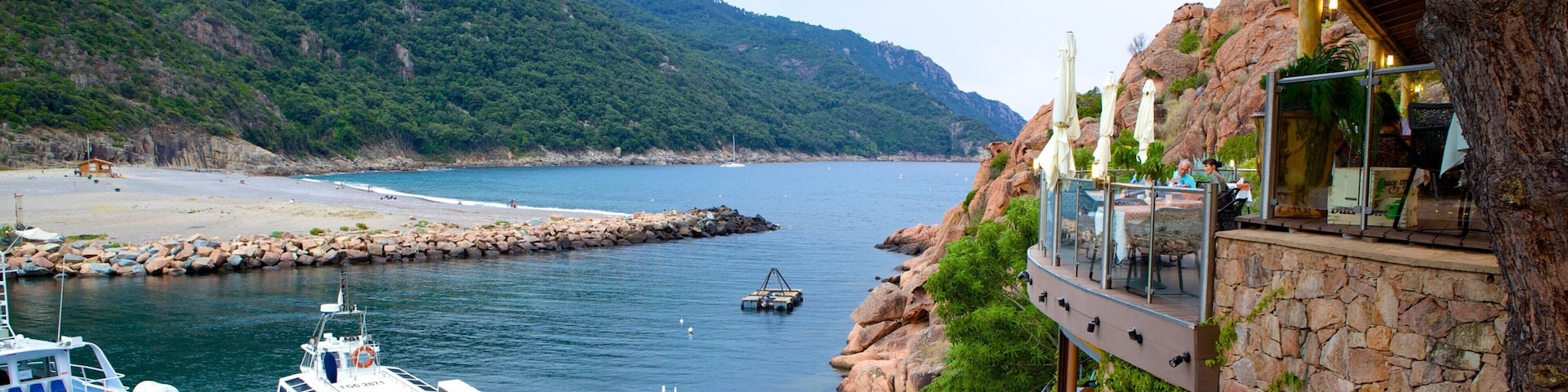 A coastal area with boats docked, a rocky shoreline, and a restaurant overlooking the sea.
