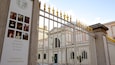 A historic building with a white facade and arched windows, surrounded by a white fence topped with golden finials.