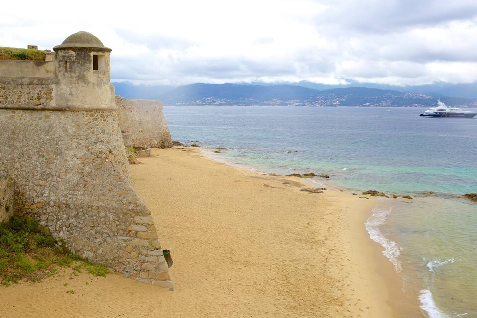 Une plage de sable avec un mur de pierres et un grand navire à l’horizon.