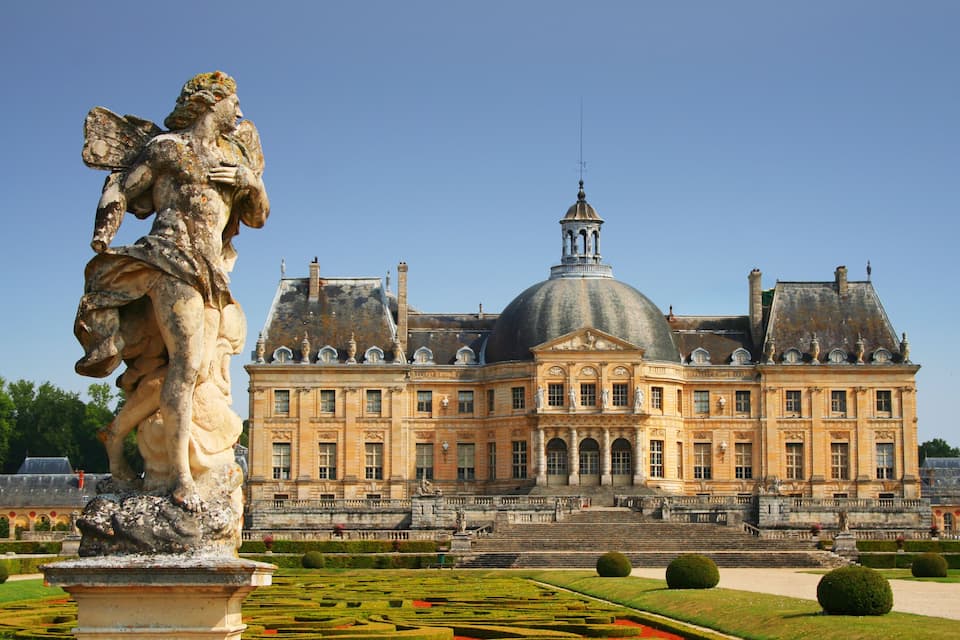 A grand historic building with a large dome and statues in a formal garden.