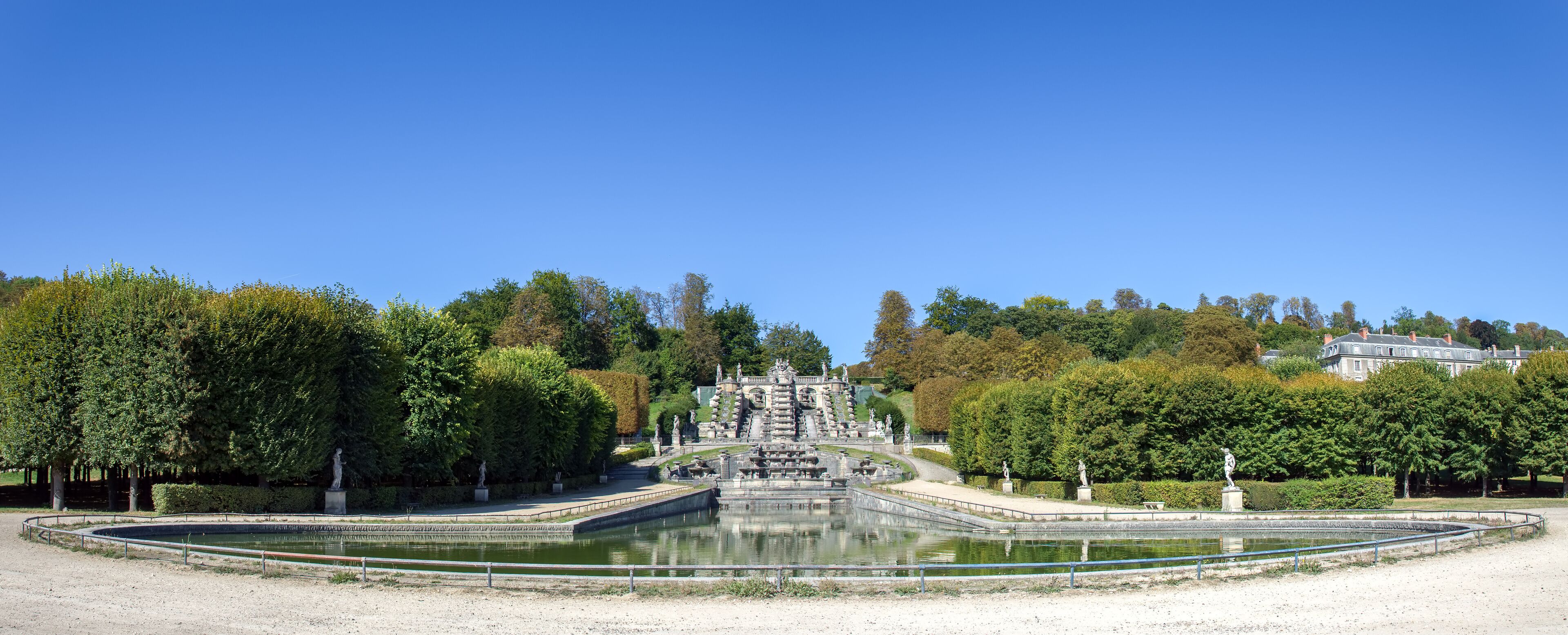 A large, ornate fountain with statues in a park with trees and a building in the background.