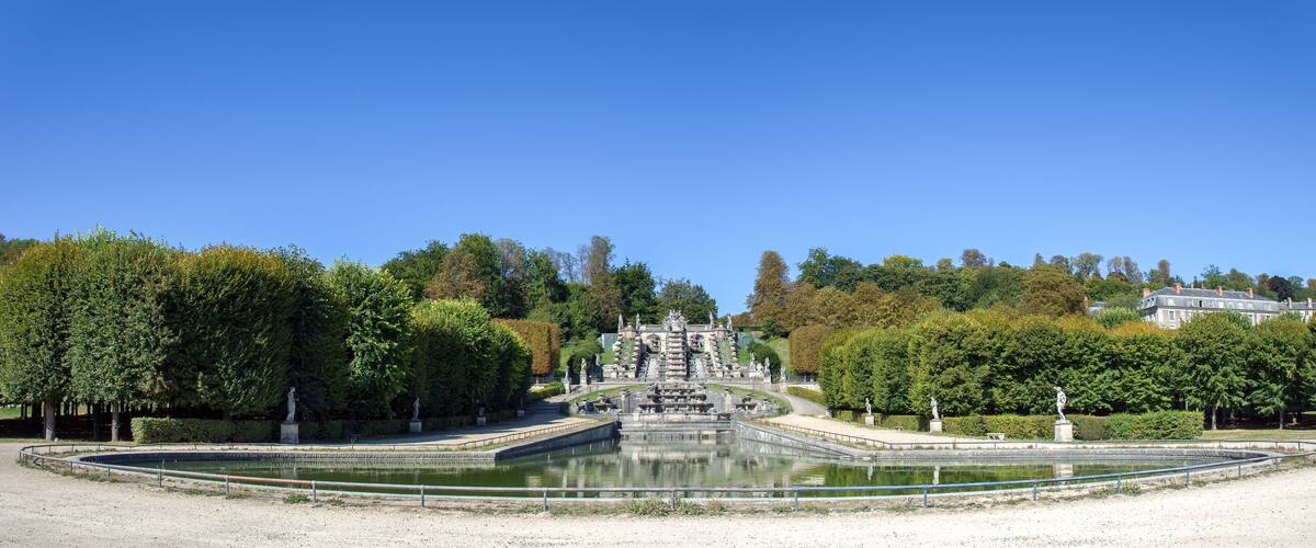 A large, ornate fountain with statues in a park with trees and a building in the background.