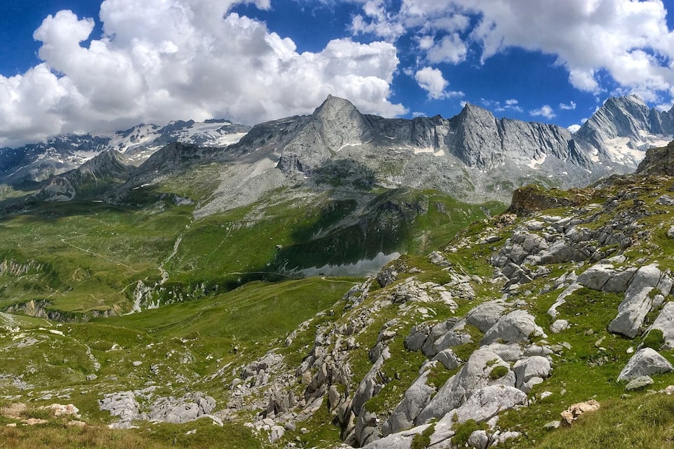A mountainous landscape with green valleys and rocky peaks under a partly cloudy sky.