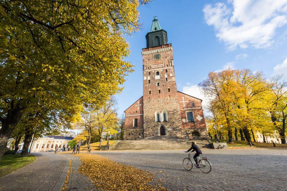 Een historisch kerkgebouw met een klokkentoren, omringd door herfstbomen en een geplaveid pad.